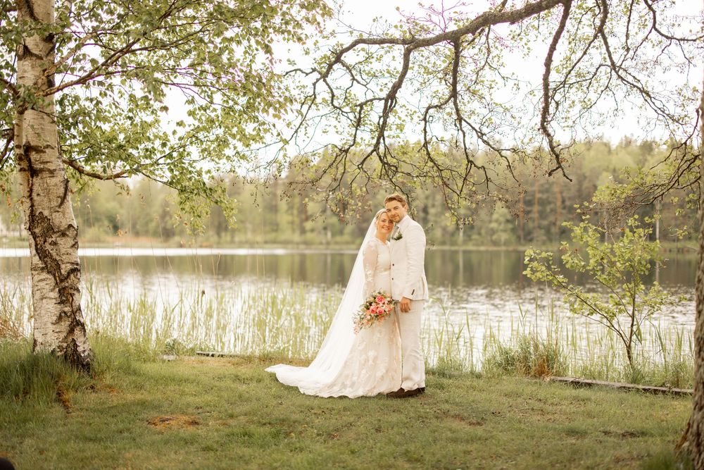 A person in an elegant white wedding gown stands near a serene lake with trees and nature in the background.