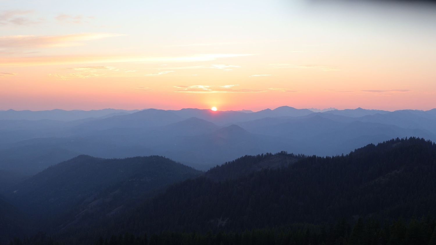 Panoramic mountain landscape at sunset with layered purple and orange hues.
