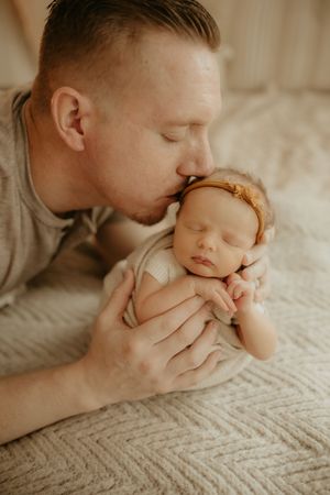 A tender moment between parent and sleeping newborn baby on a textured white blanket.