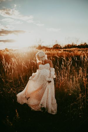 Ethereal golden hour photos of a couple in formal attire dancing through a sunlit meadow with tall grass.