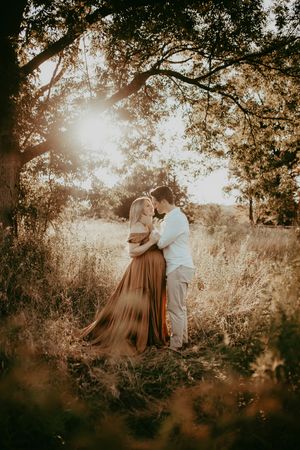 Romantic sunset maternity photos showing a couple embracing under golden-lit trees.