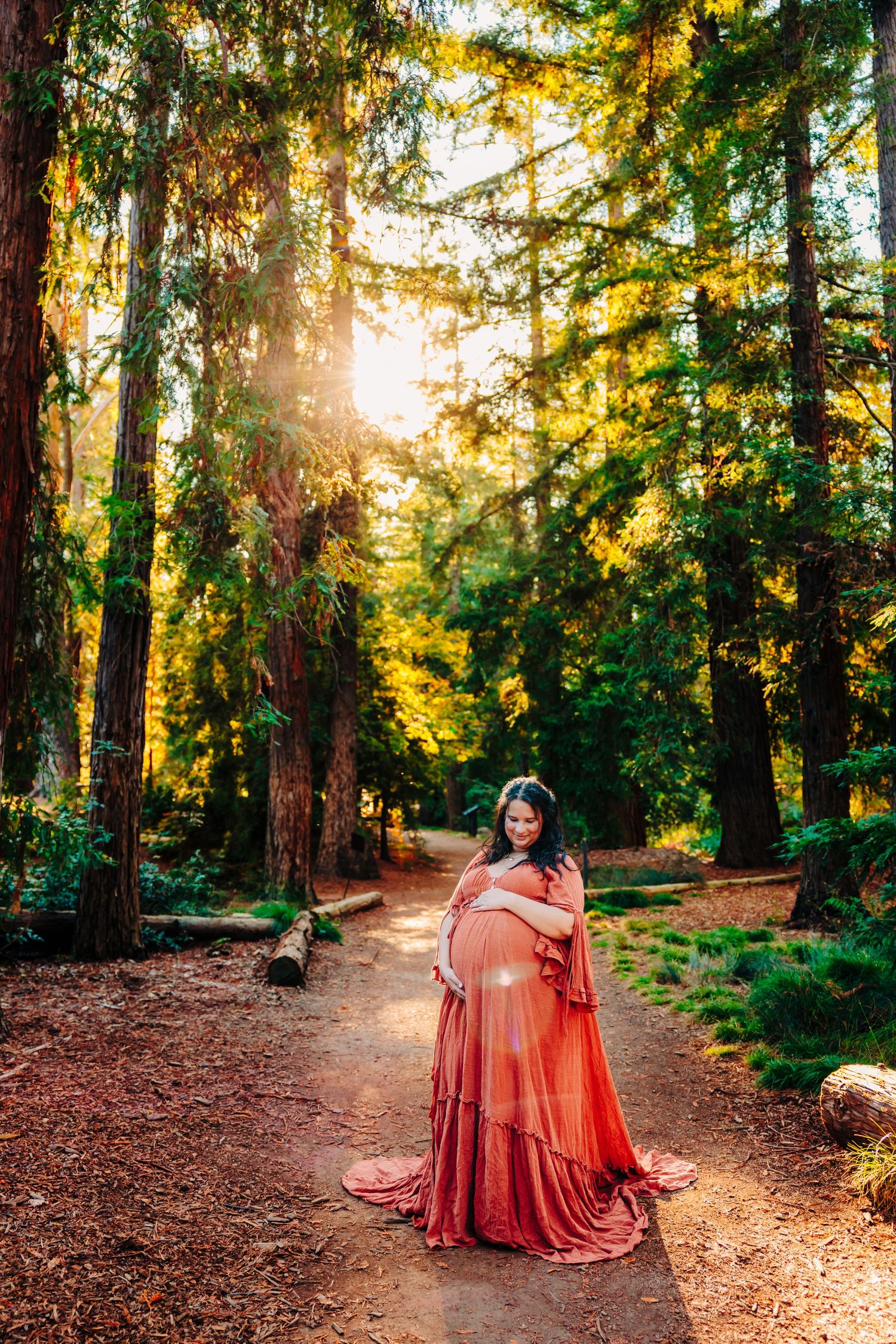 Lifestyle portrait of a woman in a flowing dress twirling along a sunlit forest path in Northern California during golden hour.