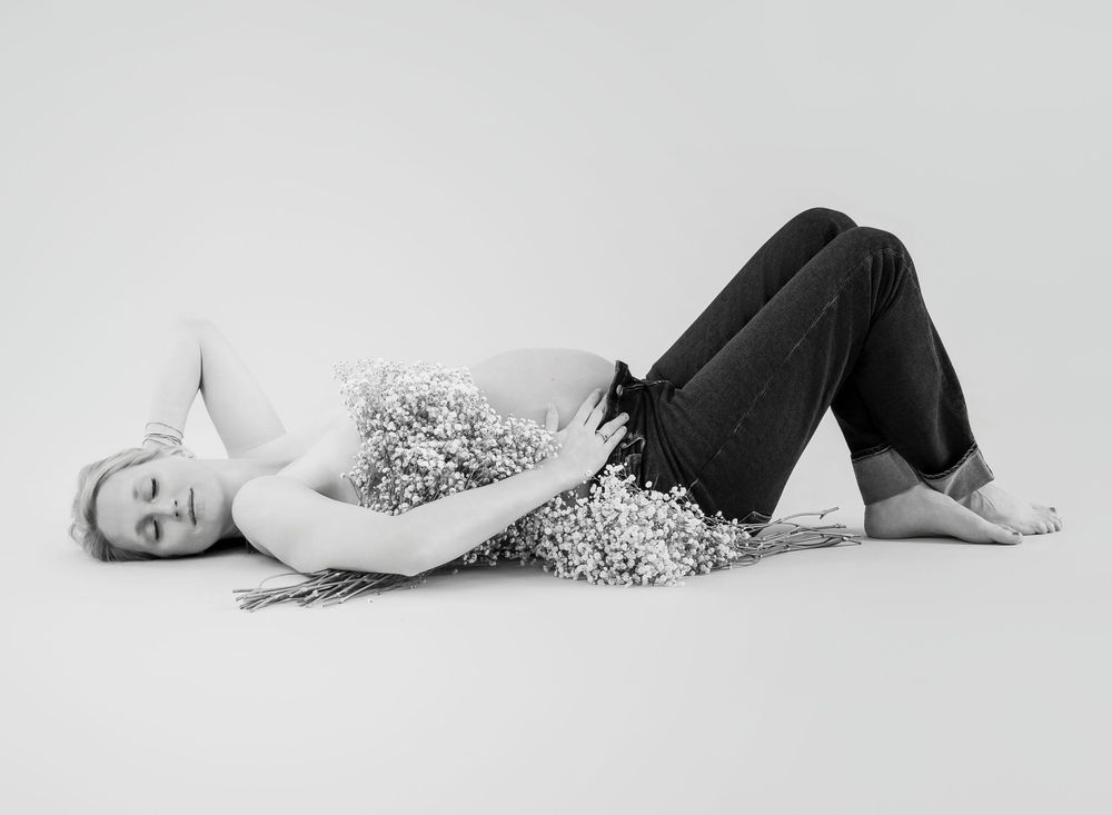 A person in a sparkly top and dark pants lies on a white floor in an artistic black and white portrait.
