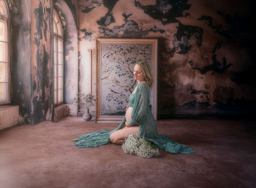 Ethereal scene in a vintage room with flowing teal dress against weathered walls and ornate framed artwork.