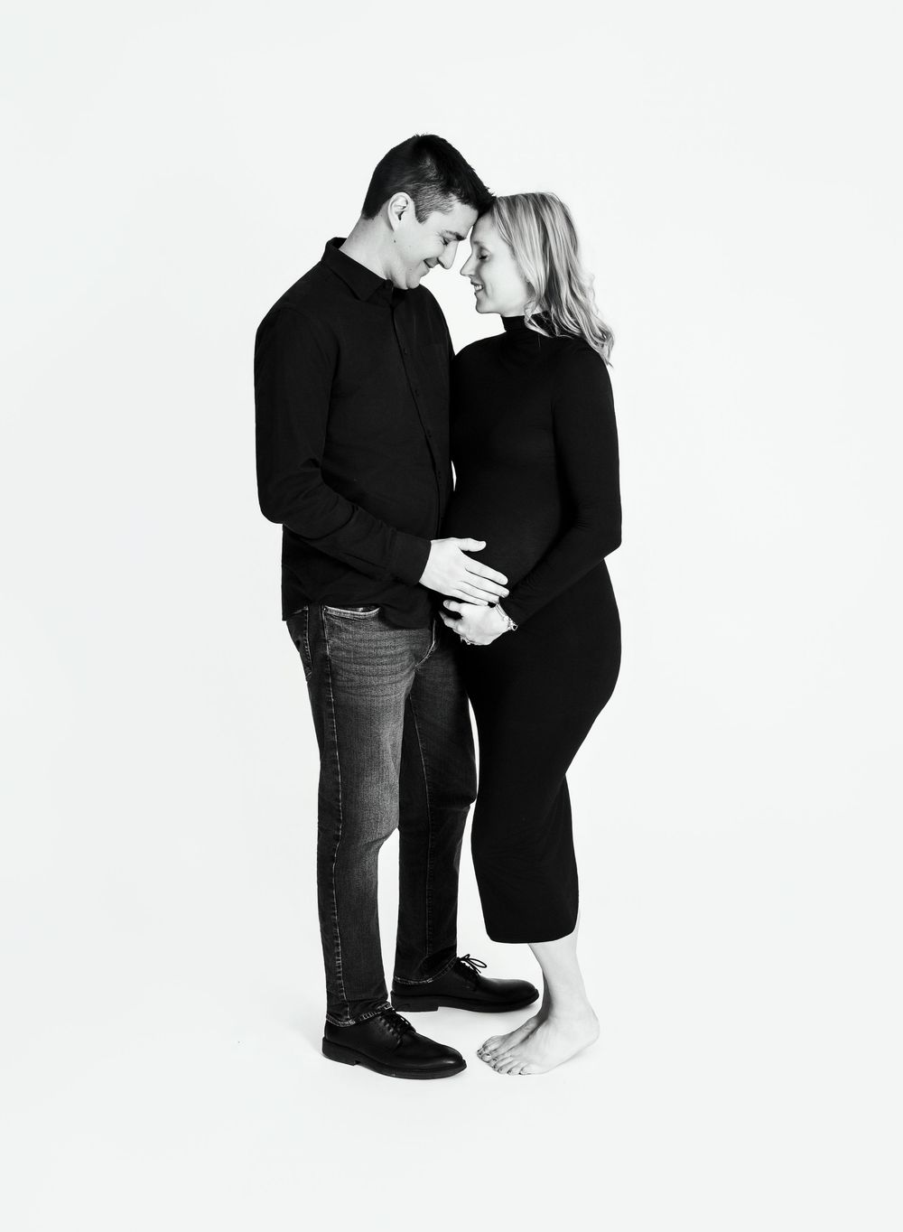 Couple in black and white clothing share an intimate moment in a minimalist studio setting.