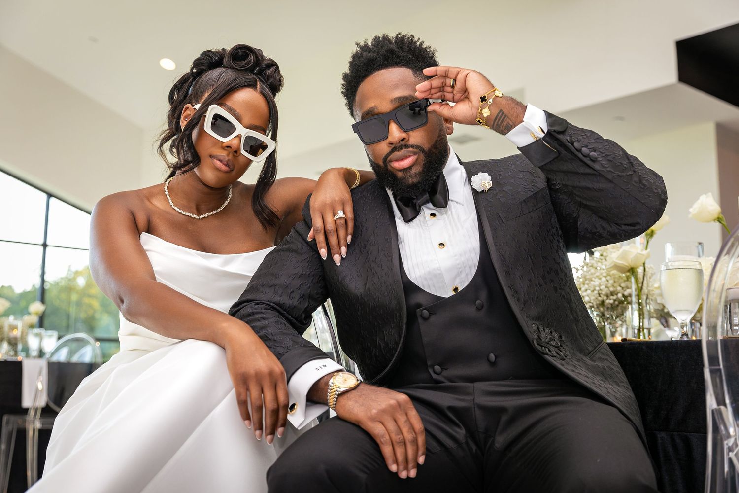 Stylish couple in wedding attire posing together, wearing sunglasses and formal wear.