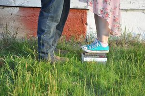 Row of legs and feet standing in green grass against white wall.