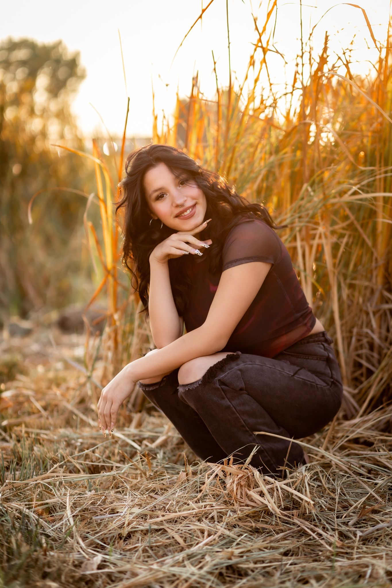 Girl poses in a black outfit among tall golden grasses during sunset, creating a warm autumn portrait atmosphere.