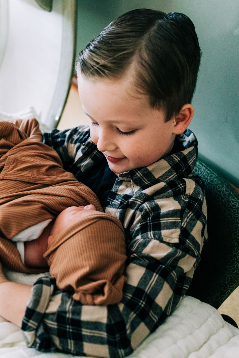 Little boy in flannel looking down holding newborn baby in the hospital, Santa Maria, CA