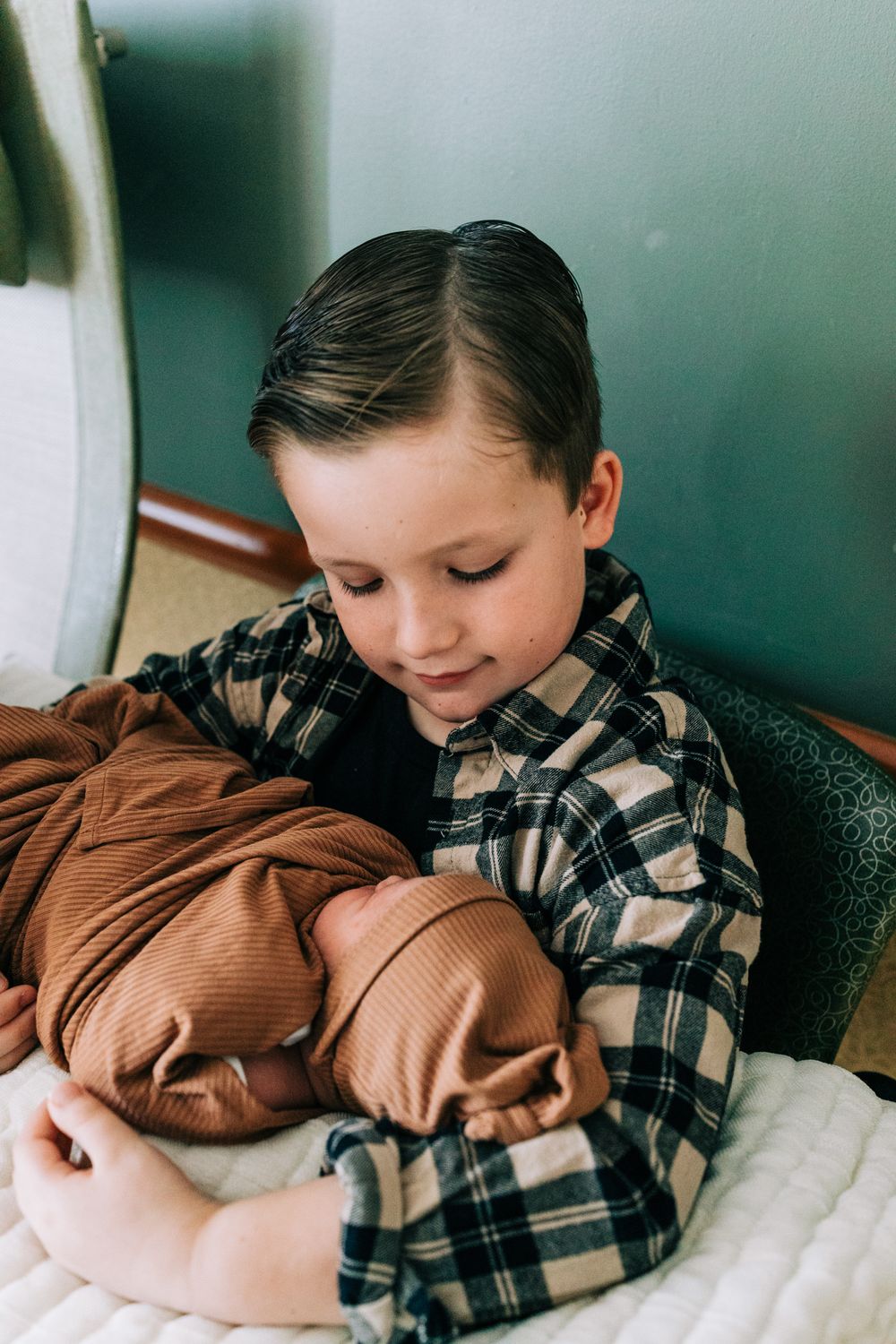 Little boy in flannel looking down holding newborn baby in the hospital, Santa Maria, CA