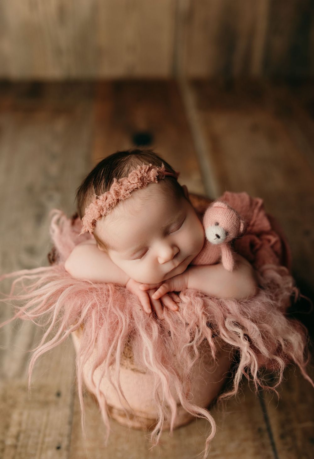 Newborn baby sleeping peacefully on soft pink fluffy blanket in artistic portrait series.