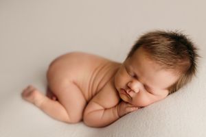 Peaceful sleeping newborn baby curled up on soft white fabric in minimalist portrait style.