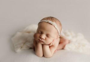 Serene newborn photography with baby sleeping peacefully on white fluffy backdrop.