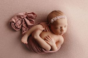 Artistic newborn photography setup with soft pink fabric and delicate wrapping.