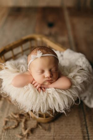Sleeping newborn on white feathered blanket in natural light newborn photography setup.