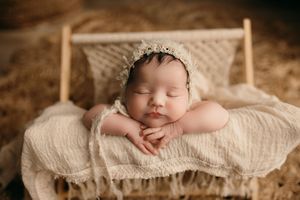 Professional newborn photography featuring sleeping baby on cream textured blanket with soft lighting.