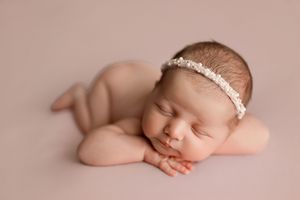 A peaceful sleeping newborn with a delicate lace headband resting on a pink backdrop during a professional photoshoot.