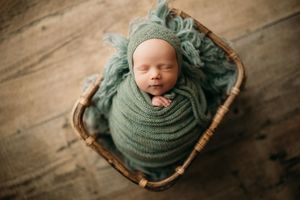 Overhead view of sleeping newborn in bamboo basket with green swaddle.