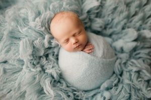 Peaceful newborn wrapped in white against turquoise textured backdrop.