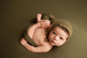 Newborn photography session with baby wearing knit bonnet in natural lighting.