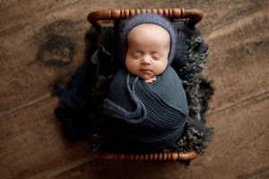 A dark wood cradle with black blankets and swaddling is photographed from above in a newborn photography setup.