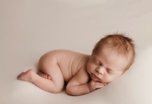 Minimalist newborn photography with baby sleeping on cream colored backdrop.