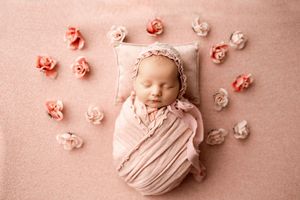 Delicate pink floral arrangement surrounding peaceful newborn on soft backdrop.