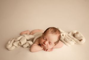 Sleeping newborn baby wrapped in soft beige fabric lying on textured backdrop in artistic composition.