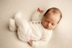 A sleeping newborn baby wrapped in soft white fabric lies peacefully on a beige textured background.