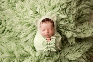 Newborn baby sleeping peacefully on soft mint green furry blanket in professional studio setting.