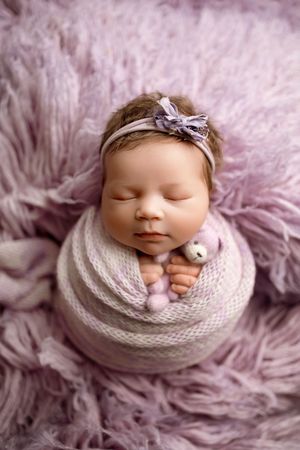 Newborn photography featuring soft purple tones and white knit wrap with silver headband accent.
