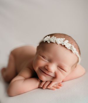 Artistic newborn portrait with delicate lace headband against neutral grey background.