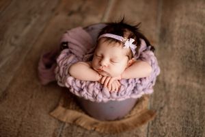 Newborn photography series with baby sleeping in pink nest on rustic wooden backdrop.