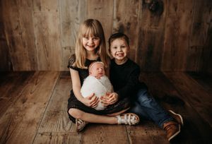 Three siblings sit together on rustic wooden floor for heartwarming family portrait.
