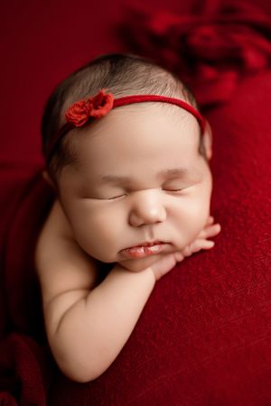 Sleeping newborn on deep red backdrop with delicate headband and peaceful expression.
