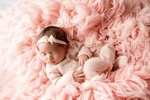 Newborn resting peacefully on soft pink textured blanket in gentle lighting.