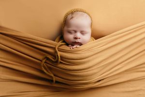 A series of seven newborn photography images showing a baby wrapped in soft beige fabric in different artistic poses.