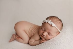 Sleeping newborn baby wrapped in white blanket lies peacefully on soft textured backdrop.