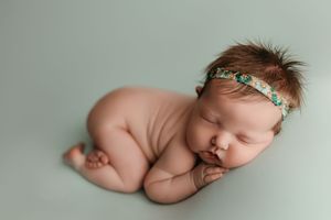 A sleeping newborn baby lies in a curled position on a soft gray background.