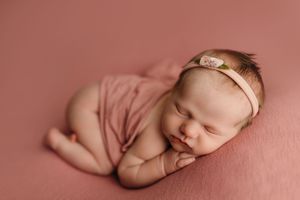 Newborn baby sleeping peacefully on soft pink blanket in natural light.
