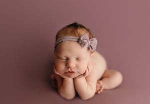 Newborn baby sleeping peacefully in fetal position on soft pink backdrop during professional photo session.