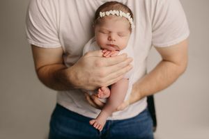 Gentle hands cradle a sleeping newborn baby against a soft white backdrop.