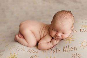 Newborn baby sleeps peacefully on personalized blanket with custom text in warm neutral tones.
