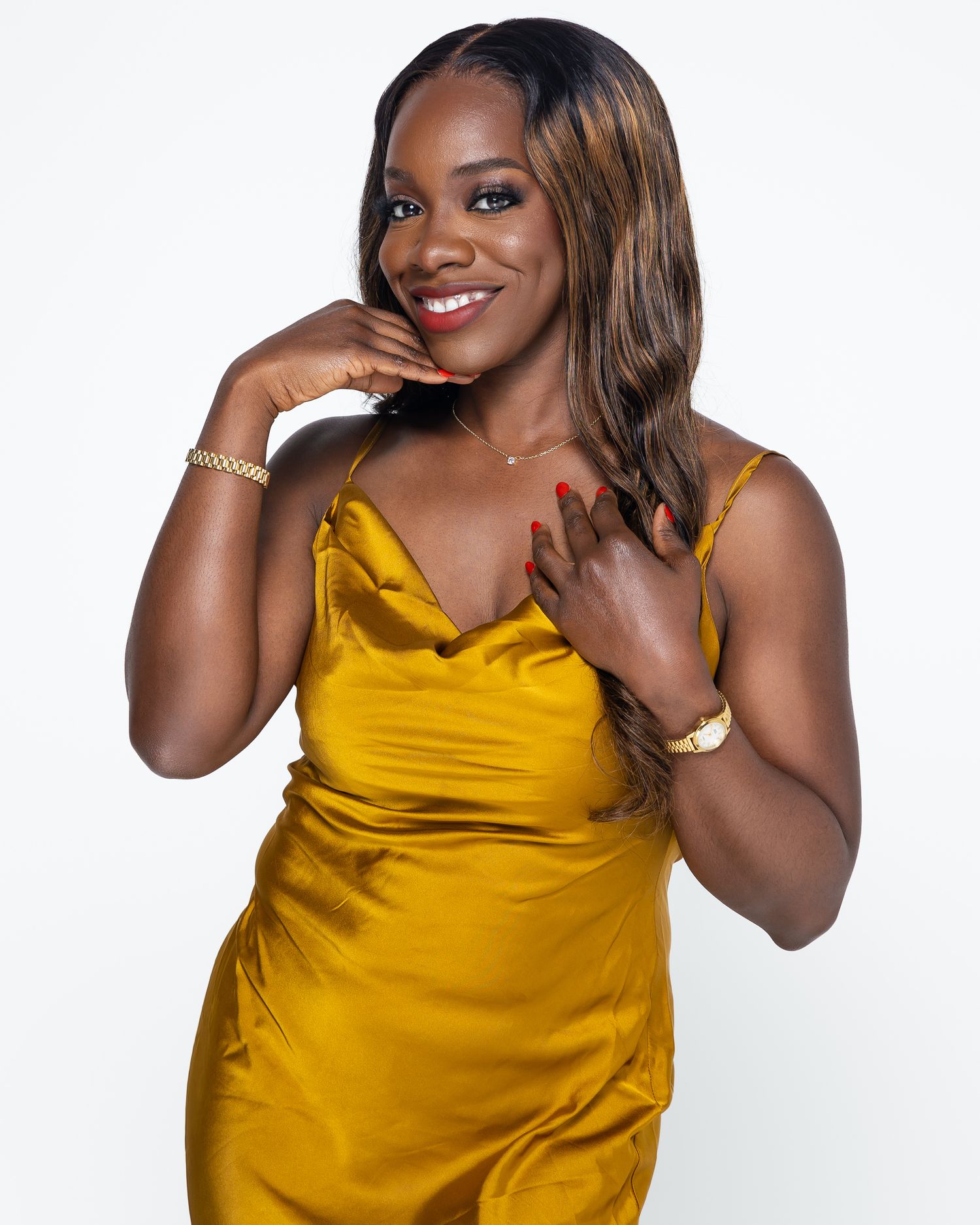 A person in a stunning mustard yellow satin dress poses against a white background with a warm, engaging smile.