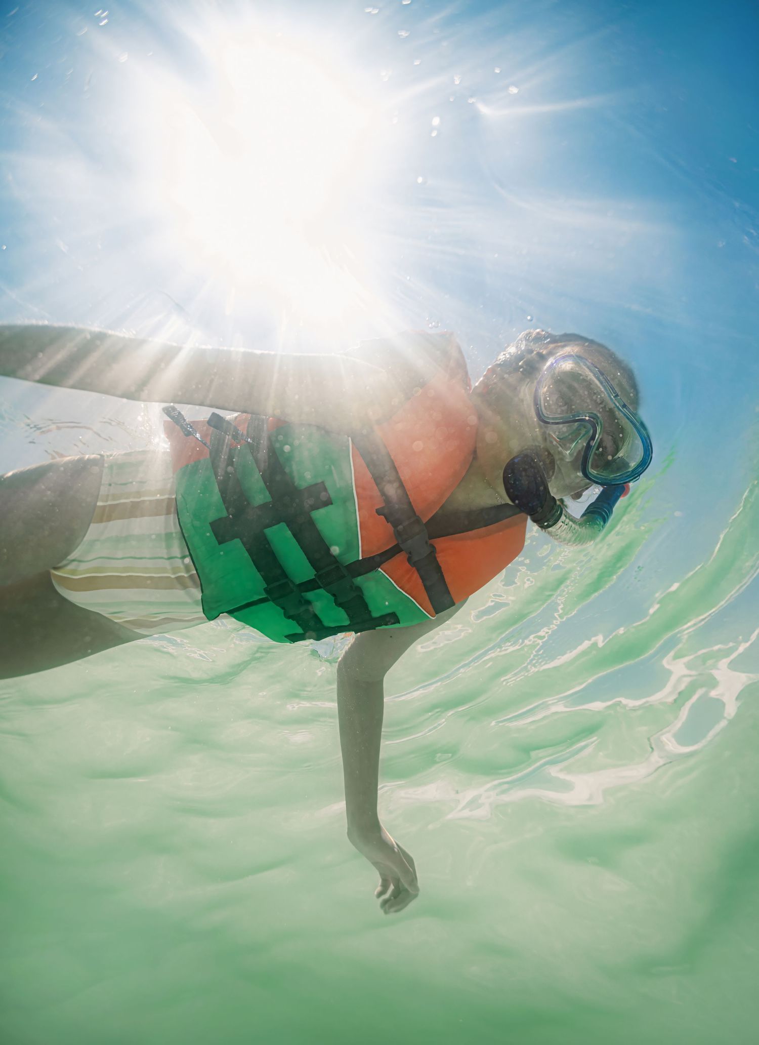Underwater view of snorkeler wearing life jacket and mask in clear shallow tropical water.