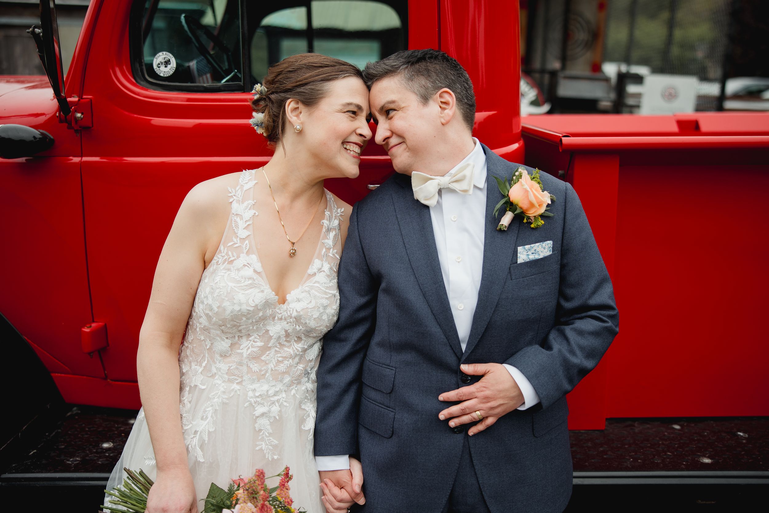 A romantic wedding couple shares an intimate moment in front of a vintage red truck.