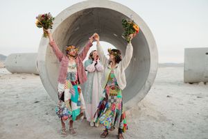 Family wearing colorful floral dresses poses playfully near concrete drainage pipe structures in desert setting.