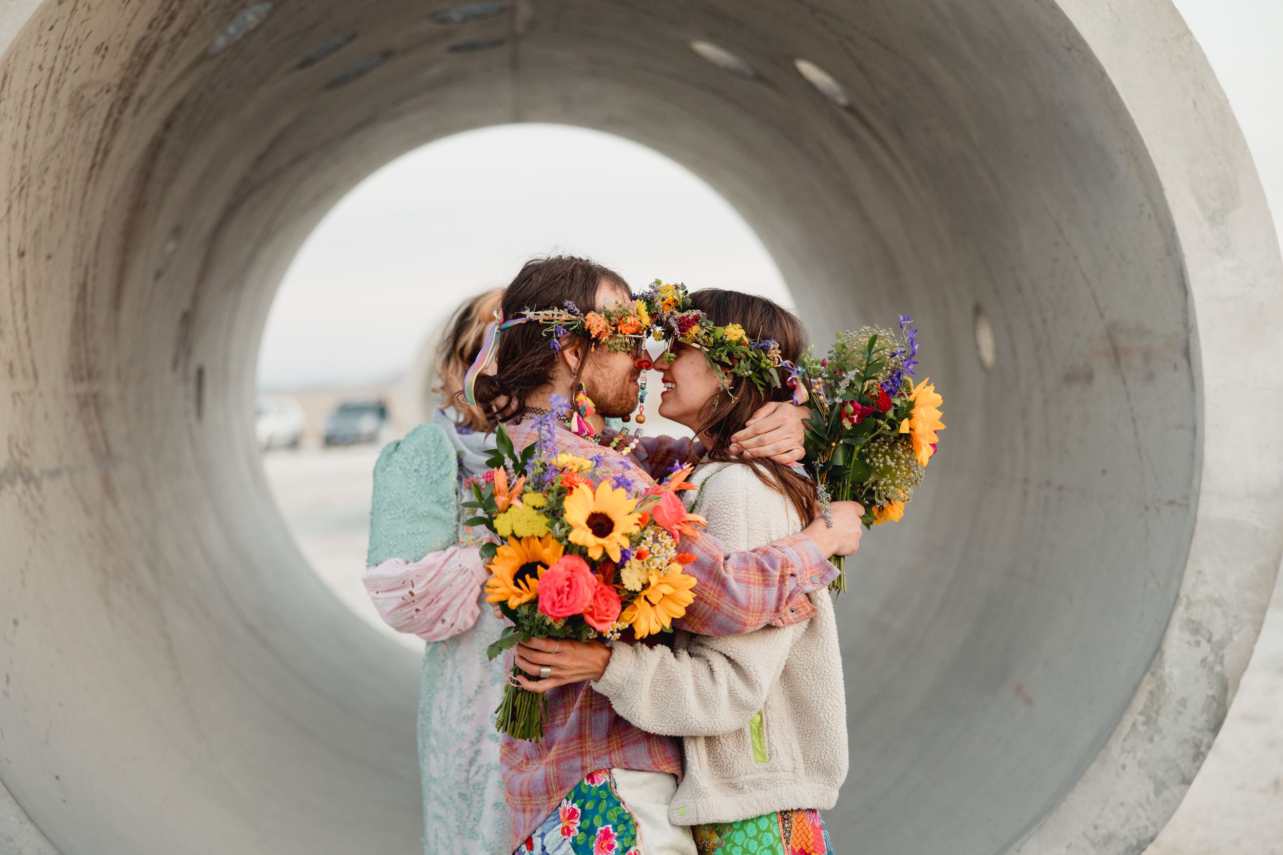 A couple sharing an intimate moment while holding vibrant sunflower bouquets inside a large concrete tunnel.