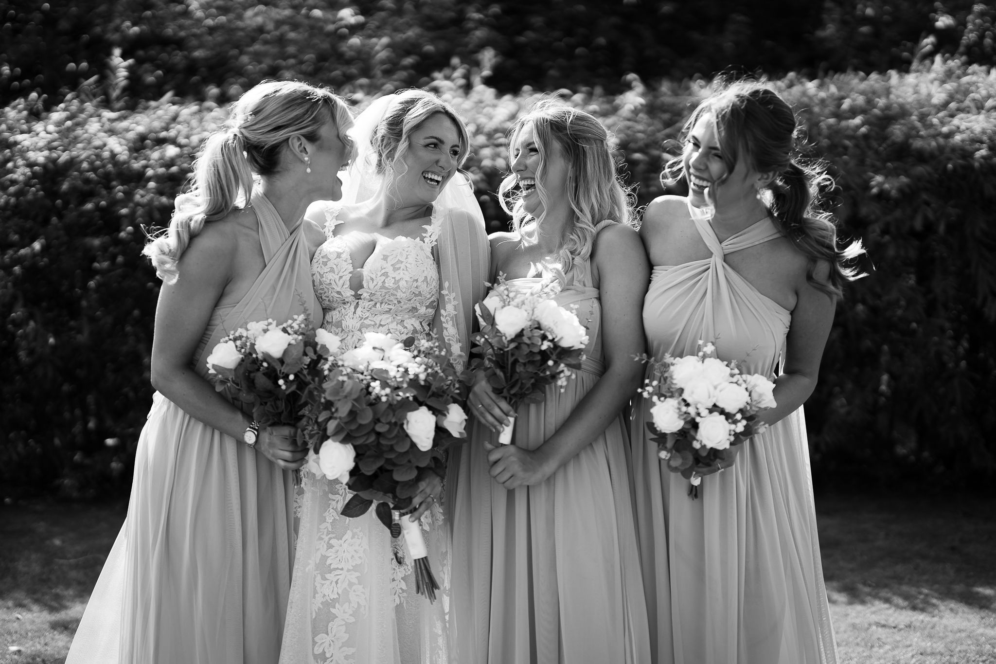 Black and white portrait of bridesmaids in matching dresses holding bouquets outdoors.