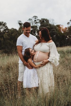 A couple in white outfits embraces tenderly in a sunlit field of tall grass during a romantic photoshoot.